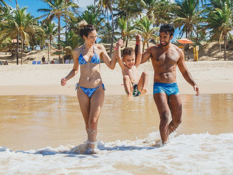 Imagem de dois adultos e uma criança se divertindo na praia
