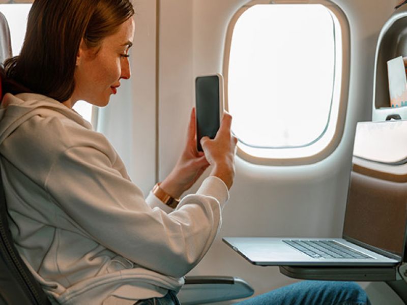 mulher mexendo no celular e notebook dentro de avião conferindo melhores blogs de viagem