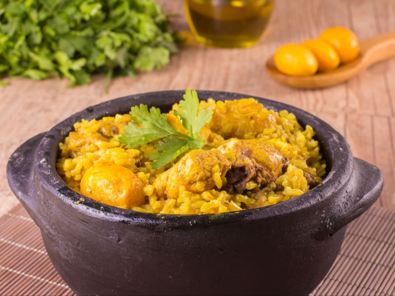 panela de arroz com frango e pequi, sobre uma esteira de madeira e uma mesa decoradas com pequi e ervas frescas