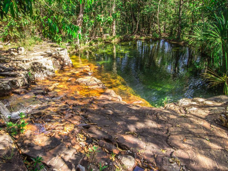 Lago na entrada de uma caverna em Goiás, com pedras em primeiro plano e vegetação de cerrado ao fundo