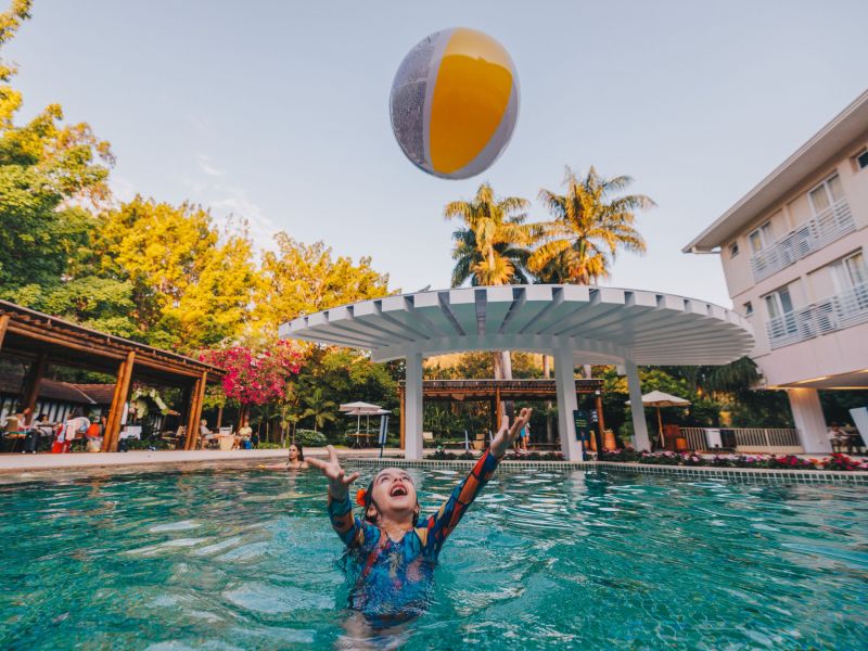 criança dentro de uma das piscinas do Rio Quente Resorts, jogando uma bola colorida para cima e sorrindo