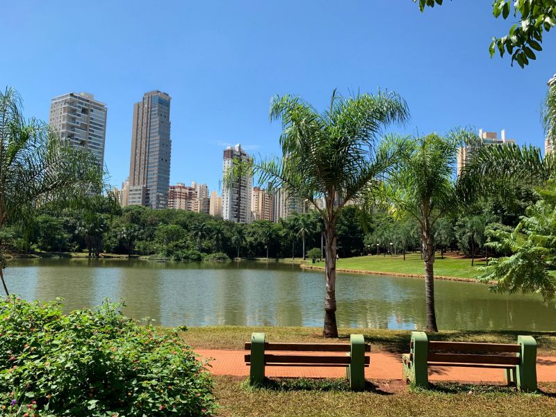 Parque Vaca Brava em Goiânia, dois bancos de praça em frente ao lago do parque, com a cidade ao final. 