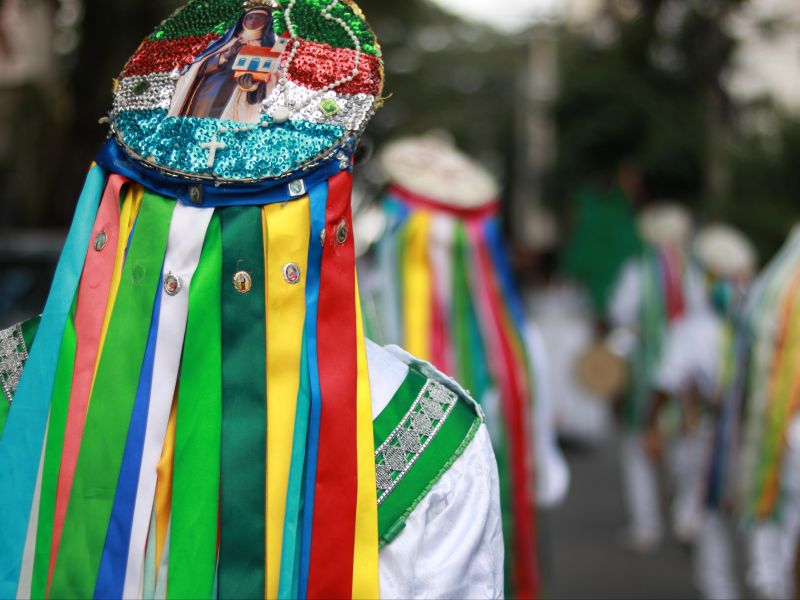 pessoa de costas usando traje típico da congada, com chapéu e fitas coloridas.