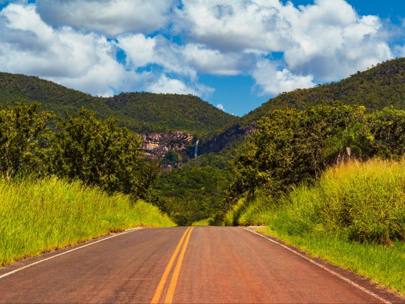 Estrada em Goiás, indo em direção a um conjunto de morros com uma cachoeira bem ao longe