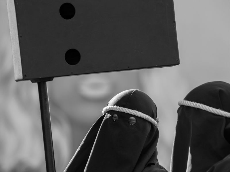 Imagem preto e branco de duas pessoas usandos as tradicionais túnicas com capuz, durante a Procissão do Fogaréu
