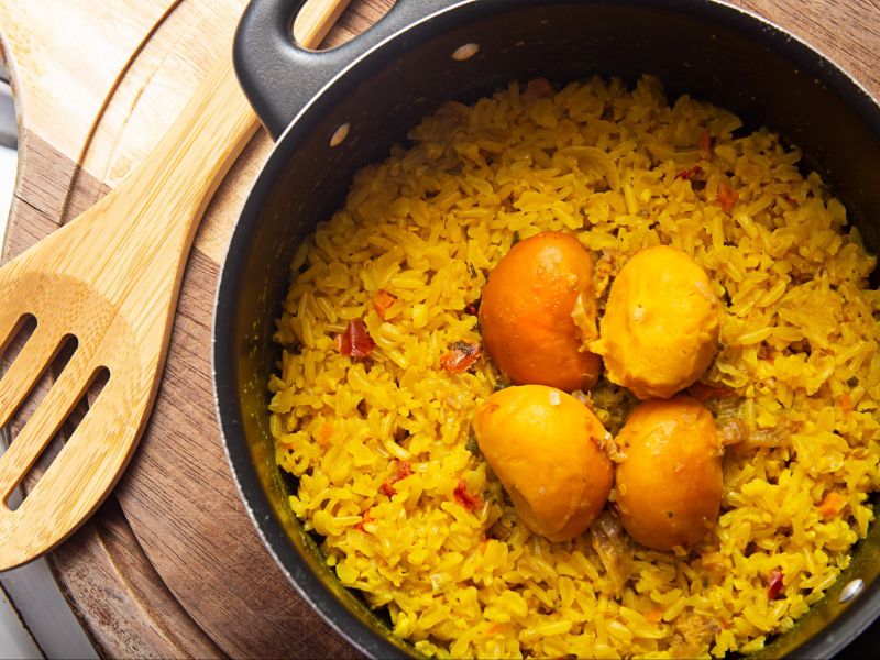 Vista de cima de uma panela de arroz com pequi e uma colher de pau ao lado